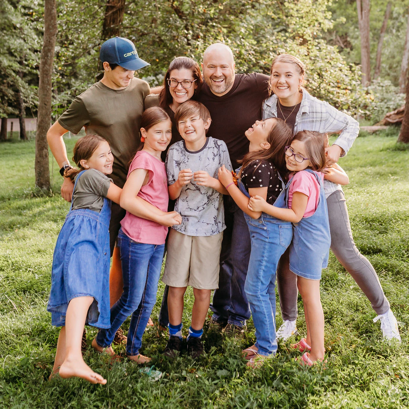 Tim and Dana Schmoyer laughing with their seven children in a sunlit field